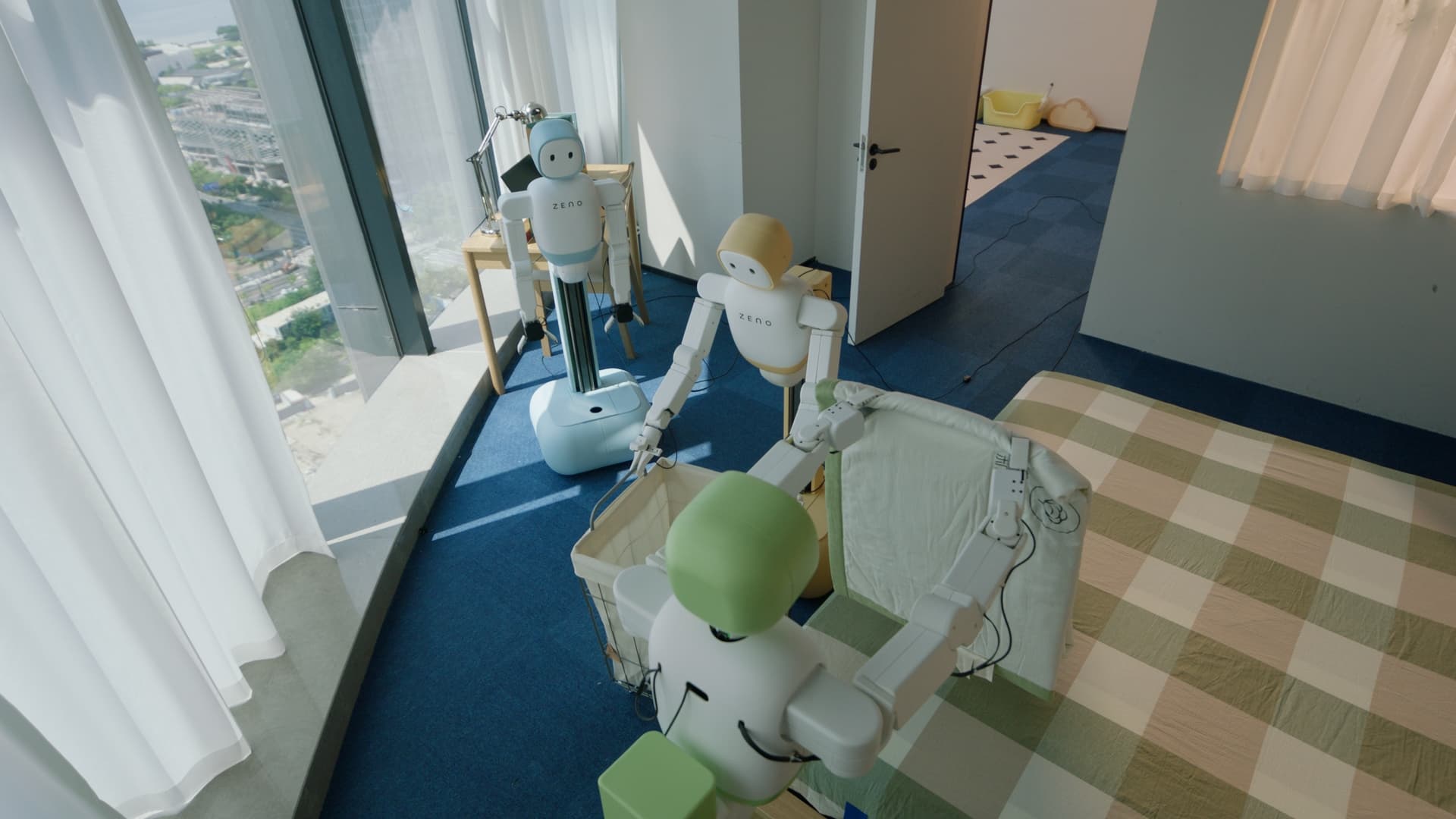 Three Zeno robots coordinating around a laundry basket beside a bed